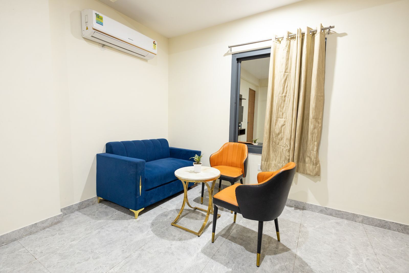 A small, modern room with a blue sofa, an orange chair, and a small table. An air conditioning unit is mounted on the wall.