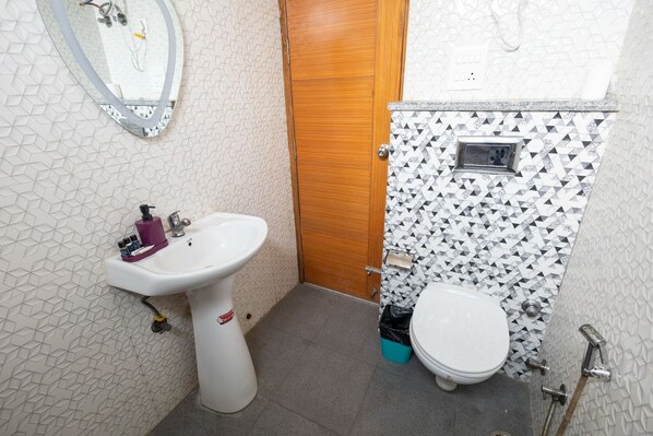 A compact bathroom with a white pedestal sink, a toilet, and a shower area. - Divine Hotels & Banquets (Noida)