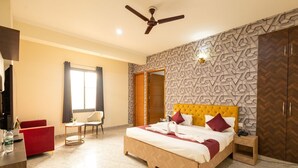 A hotel room with a bed, a desk, a chair, a TV, and a wardrobe. - Divine Hotels & Banquets (Noida)