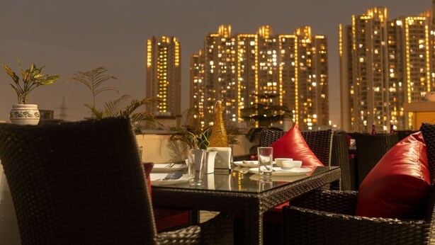 A dining area with a table set for two, featuring a city skyline view in the background. - Divine Hotels & Banquets (Noida)