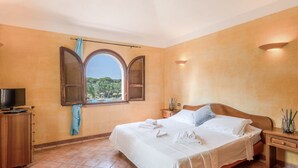A bedroom with a large bed, a TV, a window with a view of palm trees, and a wooden cabinet. - Baia delle Palme by Interhome (Pula)