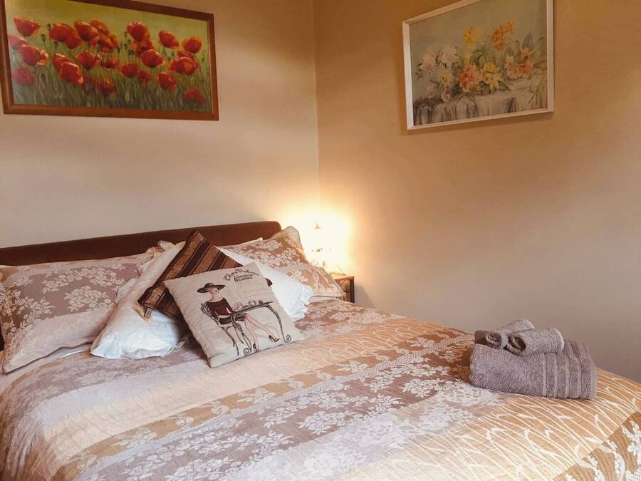 Una cama bien tendida con ropa de cama de estampado floral, una almohada decorativa y una toalla enrollada a un lado.