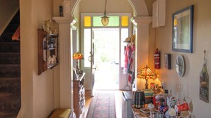A hallway with a staircase on the left, a door leading outside, and a table with various items on the right. - Anglesea House Inn (Blenheim)