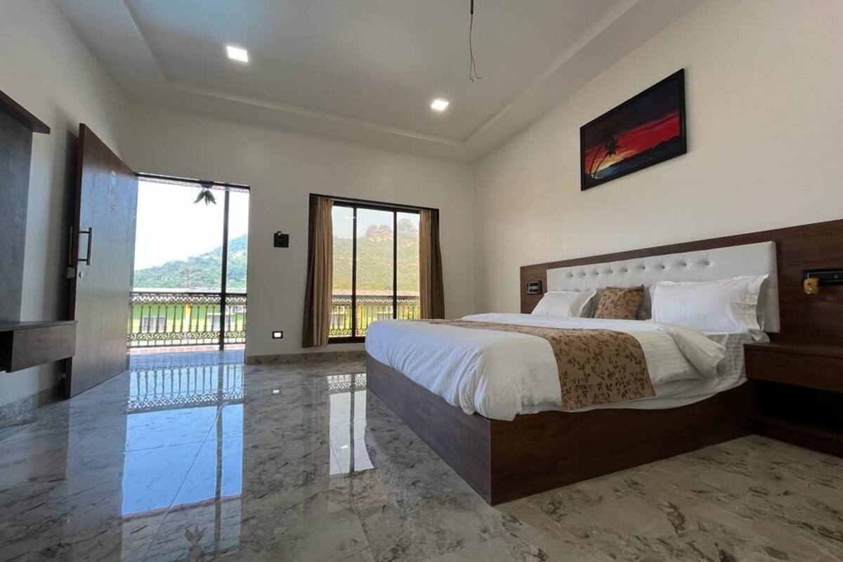 A spacious bedroom with a large bed, a television, and a balcony with a view of the mountains.