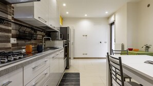 Uma cozinha moderna com fogão, micro-ondas e forno, uma sala de jantar com mesa e cadeiras, e uma porta branca ao fundo.