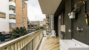 Varanda com uma banheira branca, um pequeno espaço para sentar e vista para edifícios próximos.