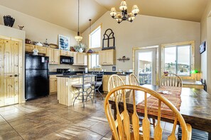Una cocina amplia con armarios de madera, un refrigerador negro y un comedor con mesa y sillas de madera.