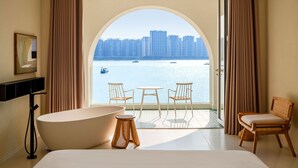 A modern bathroom with a large bathtub, two chairs, and a view of a cityscape through an arched window. - Masuland (Shantou)