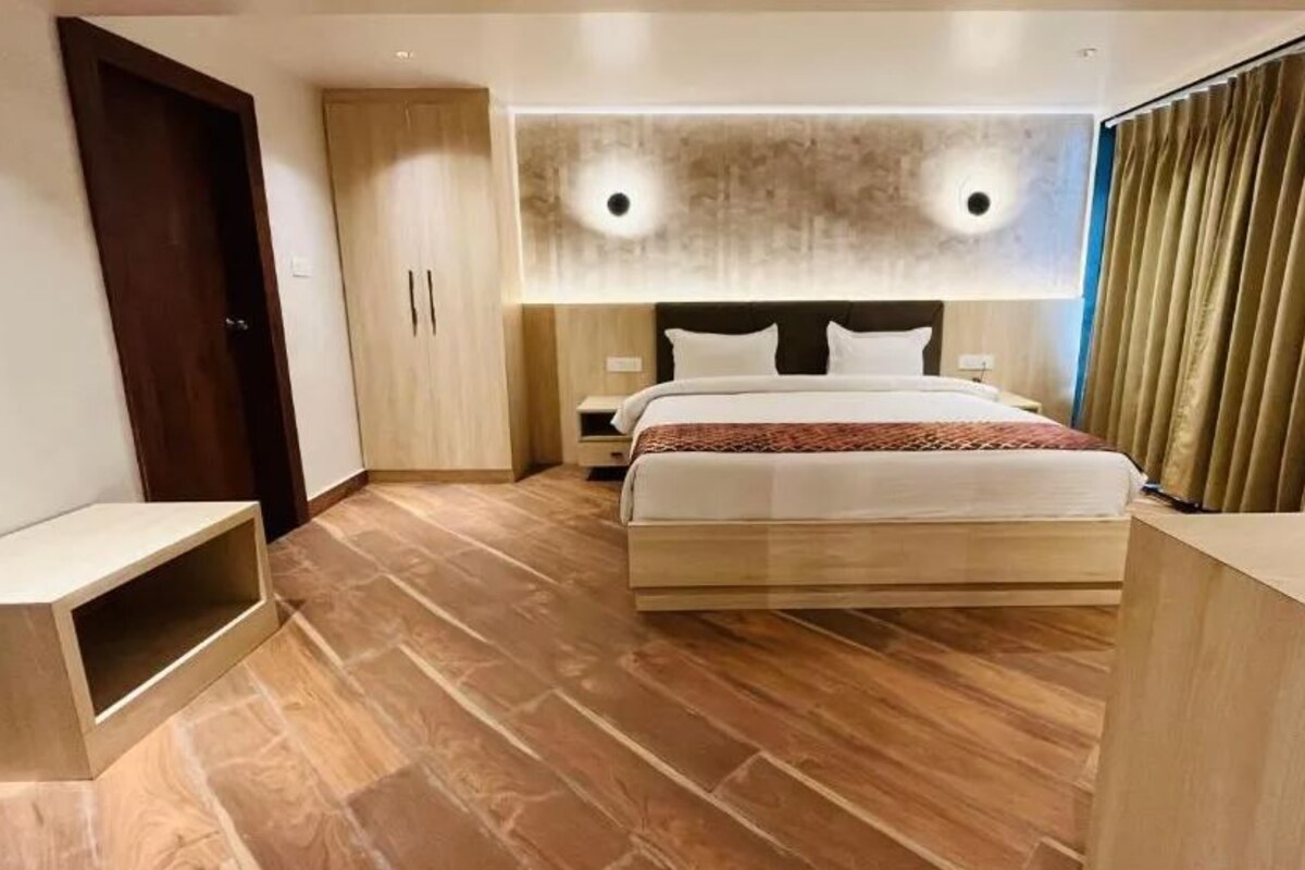 A modern hotel room with a large bed, wooden flooring, a wardrobe, and a bedside table.