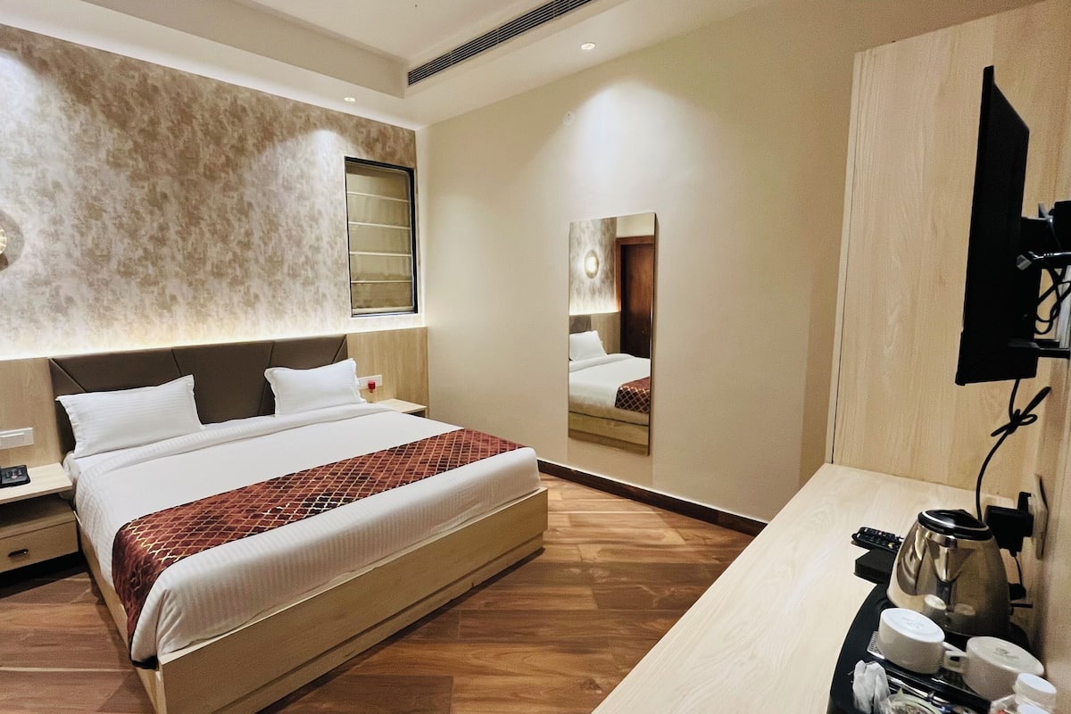 A hotel room with a large bed, a bedside table with a phone, a mirror, and a coffee station.
