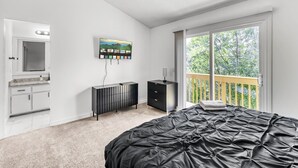 Quarto com cama, televisão, penteadeira, cômoda e varanda com vista para árvores.