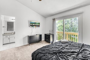 Een slaapkamer met een bed, een televisie, een dressoir, een kaptafel en een balkon met uitzicht op bomen.