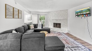 Uma sala de estar moderna com um sofá seccional, lareira, televisão montada e obras de arte nas paredes.