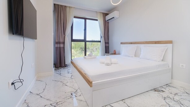 Une chambre à coucher moderne avec un grand lit, un téléviseur à écran plat fixé au mur et une vue sur la verdure.