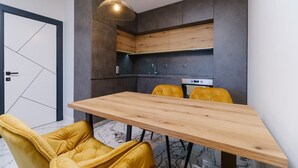 Une cuisine moderne avec des meubles de couleur sombre, un plan de travail en bois et un four encastré. On y trouve une table à manger avec des chaises jaunes.