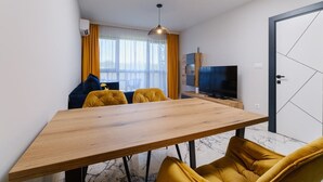 Un salon moderne avec une table à manger en bois, des chaises jaunes, un canapé, un téléviseur et une grande fenêtre avec des rideaux.