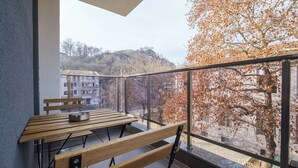 Een balkon met een houten tafel en bank, met uitzicht op gebouwen en bomen.