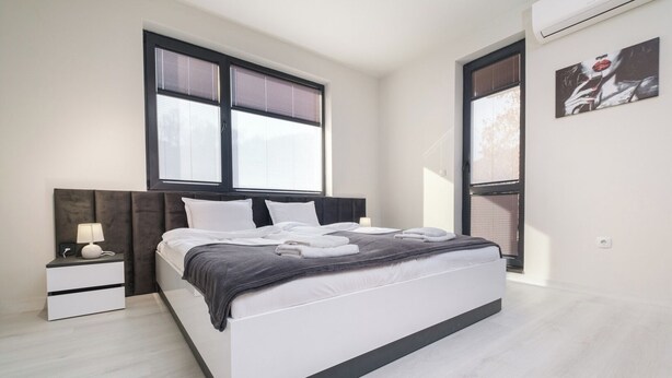 Een moderne slaapkamer met een groot bed, nachtkastjes en een raam met zonwering.