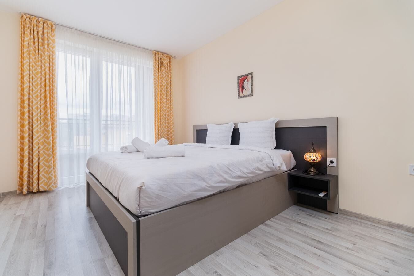 A modern bedroom with a bed, curtains, a nightstand, and a wall-mounted lamp.