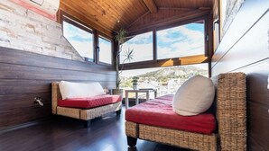 Ein gemütliches Zimmer mit zwei Korbssofas, eine mit rotem Kissen und die andere mit weißem Kissen, einem kleinen Tisch und Blick auf eine Hügelkuppe.