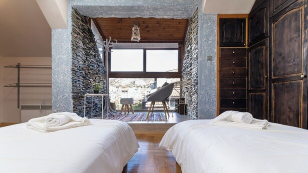 Ein Schlafzimmer mit zwei Betten, einer Steinwand, einer Holzbalkendecke und Blick auf einen Balkon mit einem Stuhl.