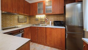 A kitchen with wooden cabinets, a stainless steel refrigerator, a microwave, and a brick backsplash.