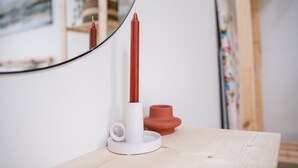 A candle holder with a red candle on a wooden table, a white candle holder, and a small red pot.