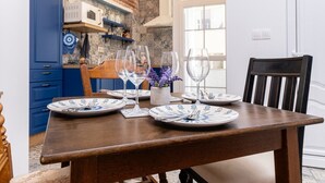 A dining table set with plates, cutlery, and wine glasses, with a brick wall and blue cabinets in the background.