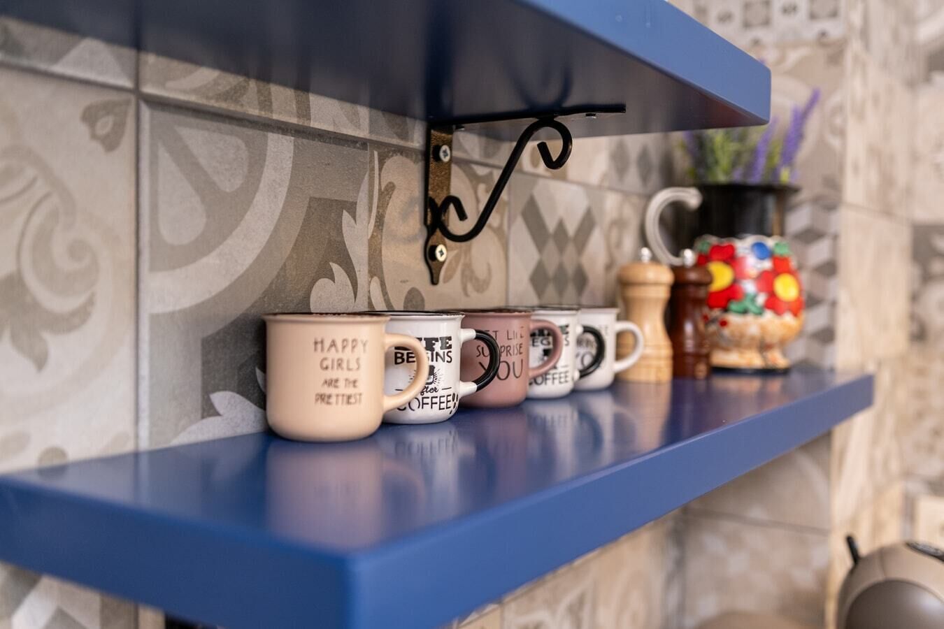 A blue shelf with a metal hook holding a small item, and a row of coffee mugs with text on them.