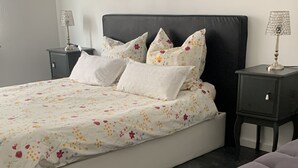 A bedroom with a bed, a nightstand, a lamp, and a large purple sofa. - Accogliente appartamento (Wuppertal)