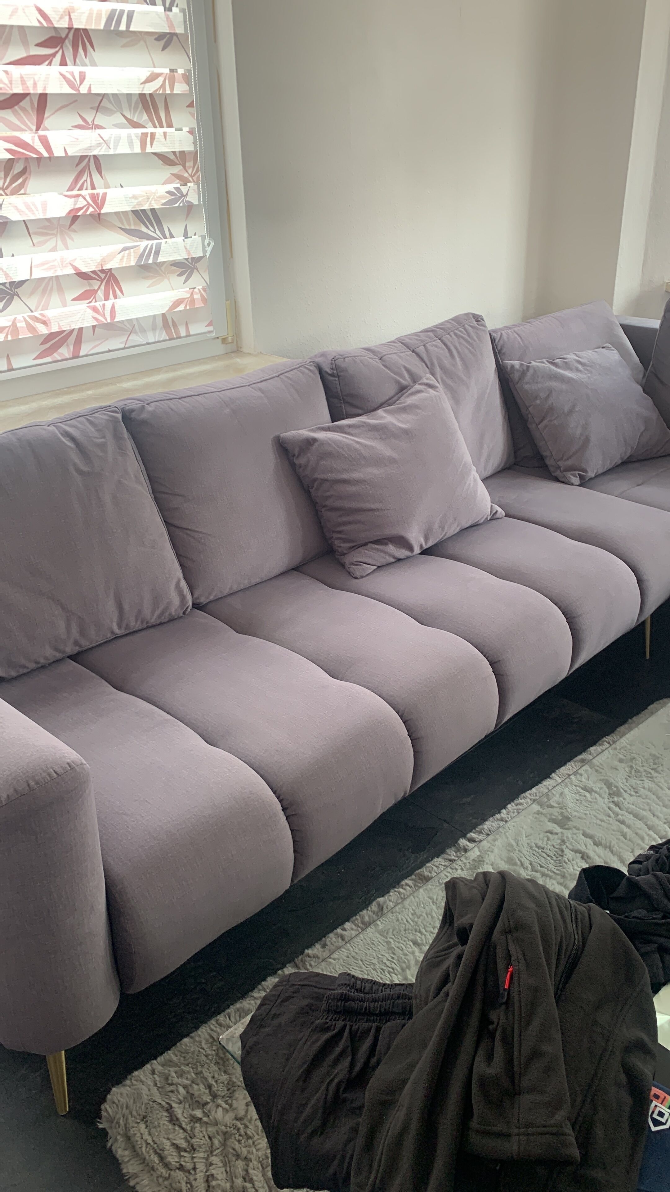 Ein graues Sofa mit vielen Kissen, eine TV-Konsole mit schwarzem Rahmen und ein weißer, flauschiger Teppich.