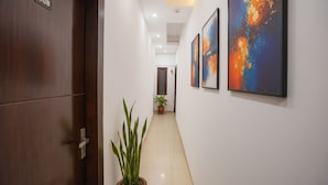 A hallway with a wooden door labeled "108", a potted plant, and three abstract paintings on the wall. - Fabexpress Prime Inn (Prayagraj)