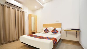 A hotel room with a bed, a bedside table, a mirror, and a shelf. - Fabexpress Prime Inn (Prayagraj)