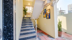 A staircase with a metal railing leading to a landing. There are two potted plants on the landing, and a wall with two framed artworks. - Fabhotel Rk Suites (Hyderabad)