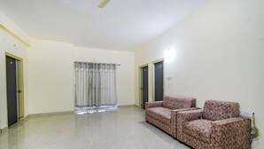 A spacious room with a patterned sofa, a curtain, and a door. - Fabhotel Rk Suites (Hyderabad)