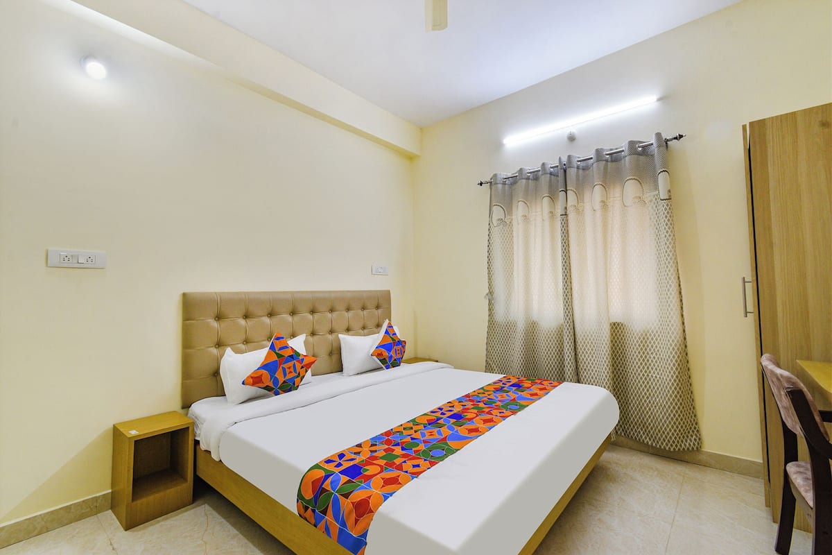 A bedroom with a bed, a nightstand, a wooden wardrobe, and a window with curtains.