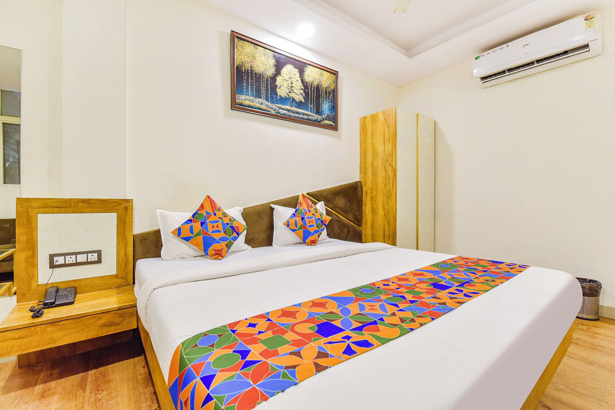 Habitación de hotel con cama, escritorio con teléfono, un cuadro en la pared y aire acondicionado.