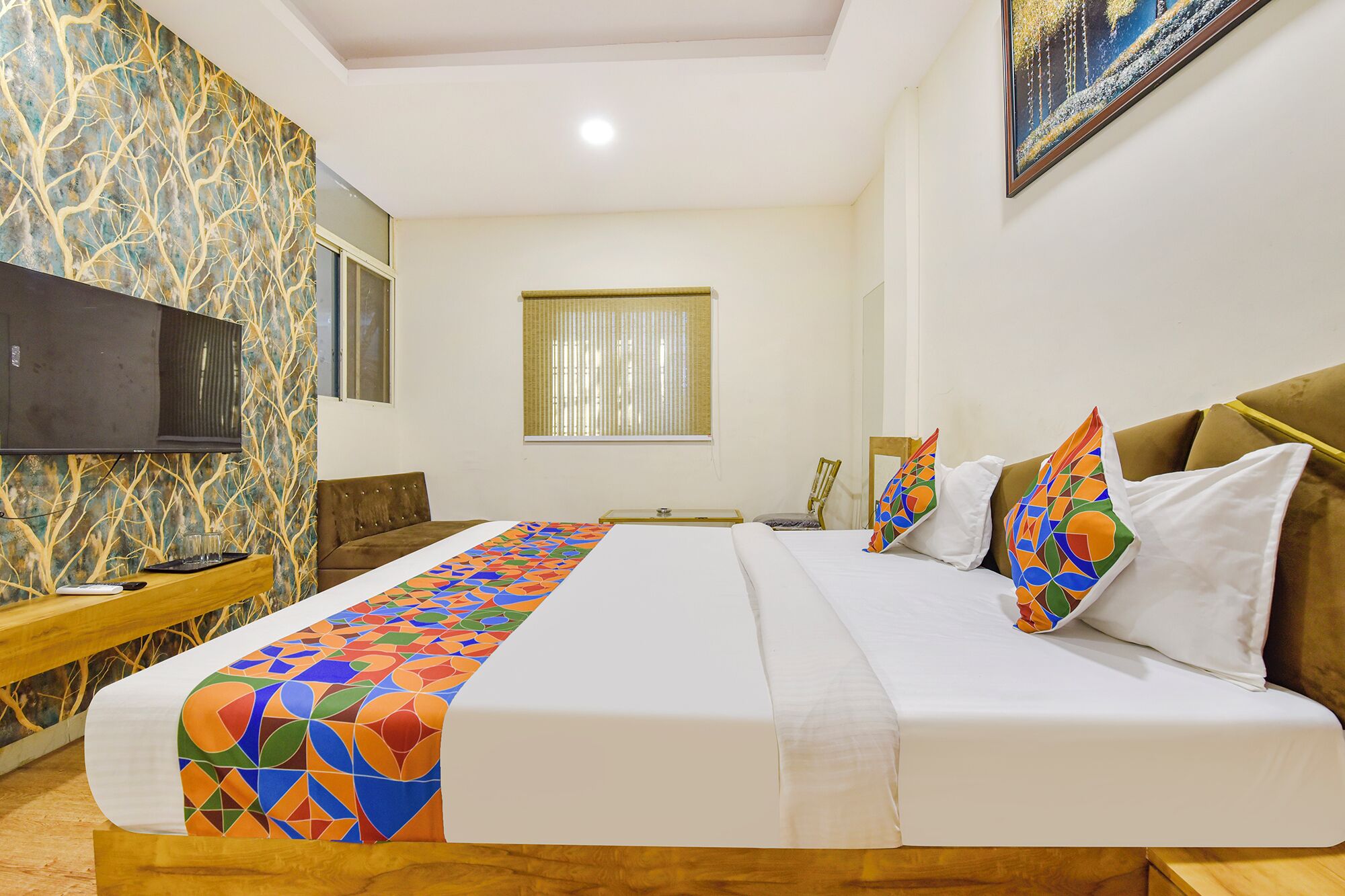 Una habitación de hotel con cama, televisión, ventana y pared con diseño geométrico.