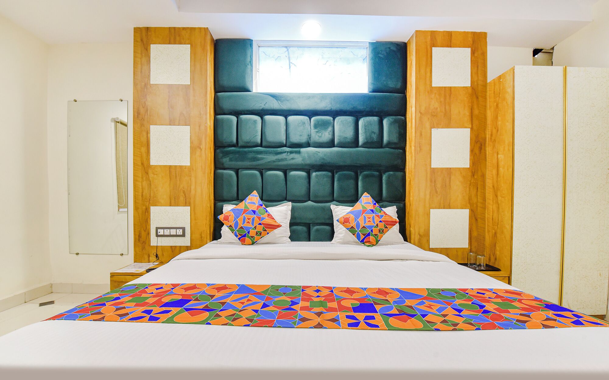 Un dormitorio moderno con una cama grande, cabecera de madera y colcha de diseño geométrico y colores vivos.