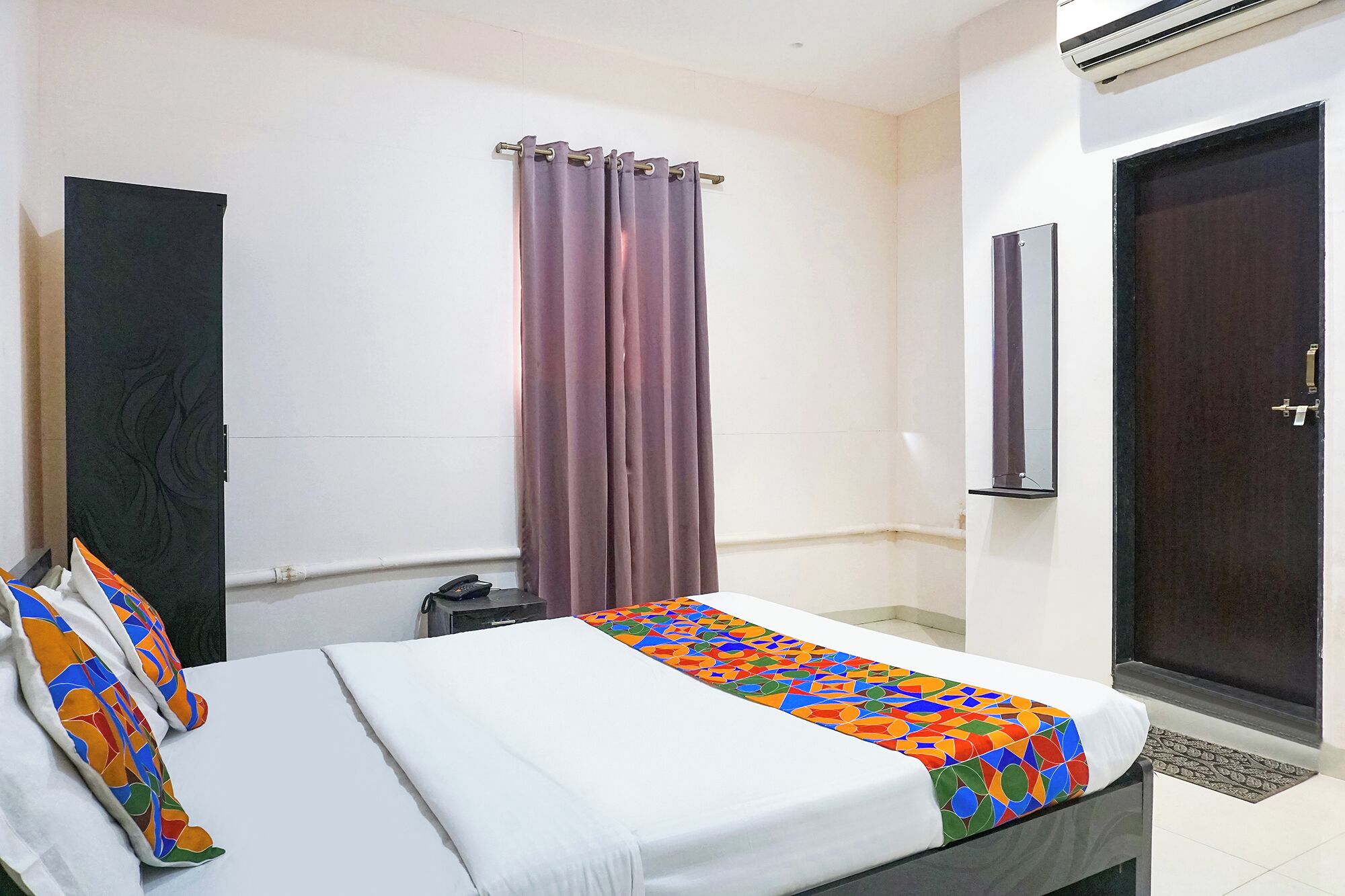 Une chambre d’hôtel avec un lit, une porte de salle de bain, un appareil de climatisation et une fenêtre avec des rideaux.