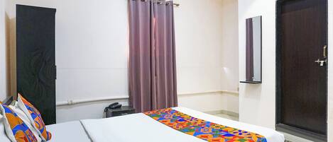 A hotel room with a bed, a bathroom door, an air conditioning unit, and a window with curtains.