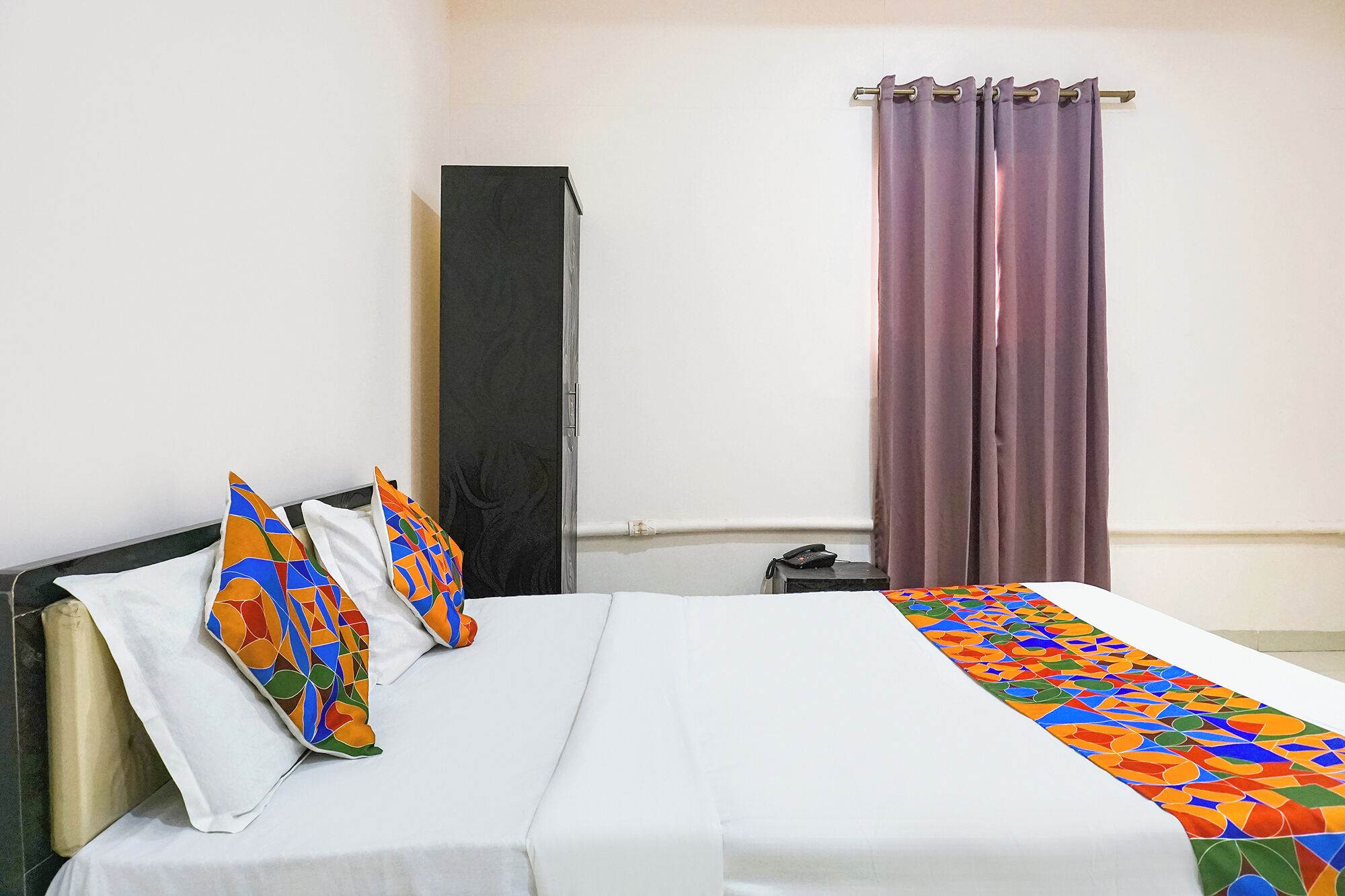 Une chambre d’hôtel avec un lit, une armoire, un téléphone et une fenêtre avec des rideaux.