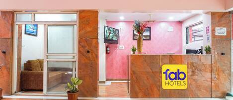 A hotel reception area with a marble reception desk, a television mounted on the wall, and a reception sign.