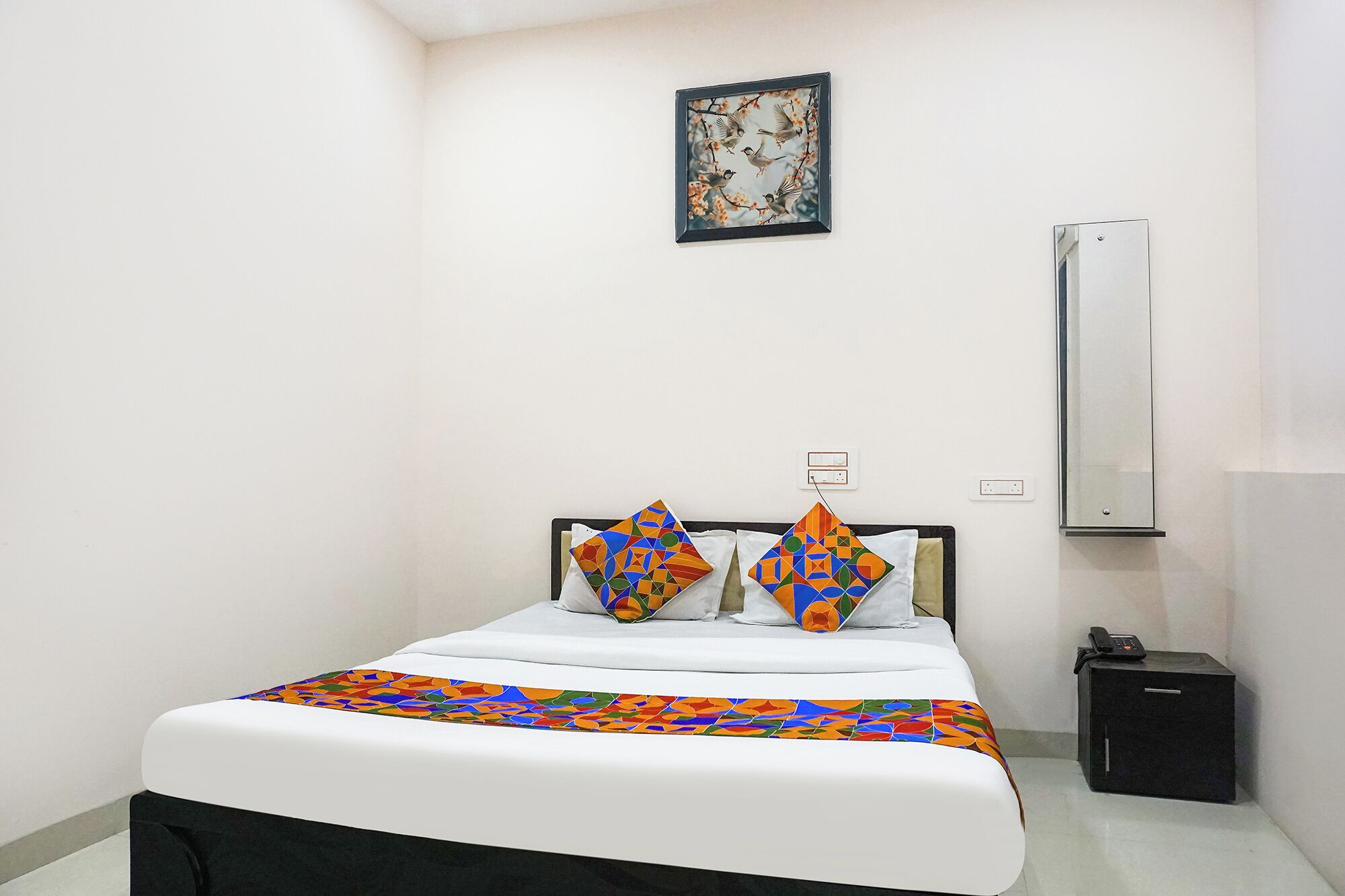 A hotel room with a bed, two pillows, a bedside table, a telephone, and a wall-mounted air conditioner.