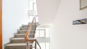 A staircase with a wooden handrail leading to a second floor, a sign indicating the floor, and a view of the outside through a window. - Fabhotel Ar Suites (Gurugram)
