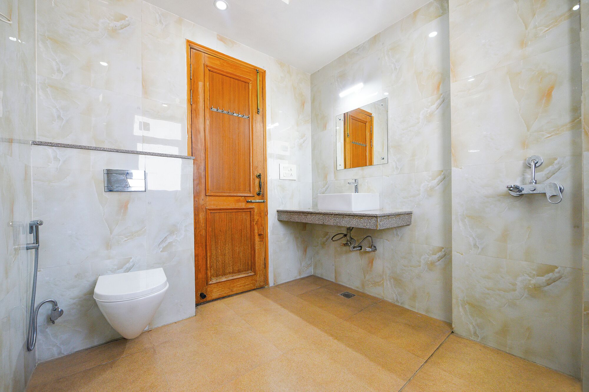 A bathroom with a wooden door, a white toilet, a sink with a mirror above it, and a shower area.