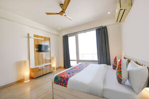 Ein Hotelzimmer mit Bett, Fernseher an einer Holzvertäfelung, Deckenventilator und Klimaanlage.