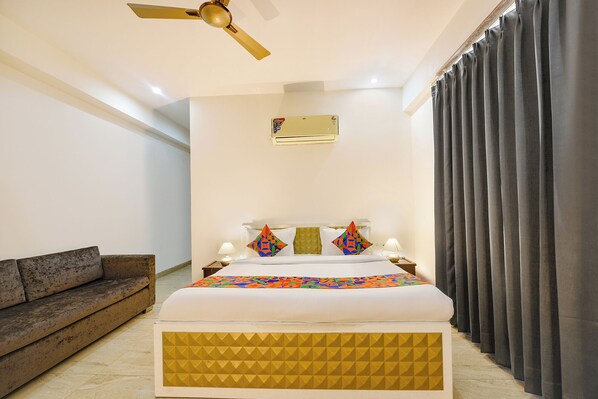 A hotel room with a bed, a ceiling fan, an air conditioning unit, a sofa, and curtains. - Fabhotel Ar Suites (Gurugram)