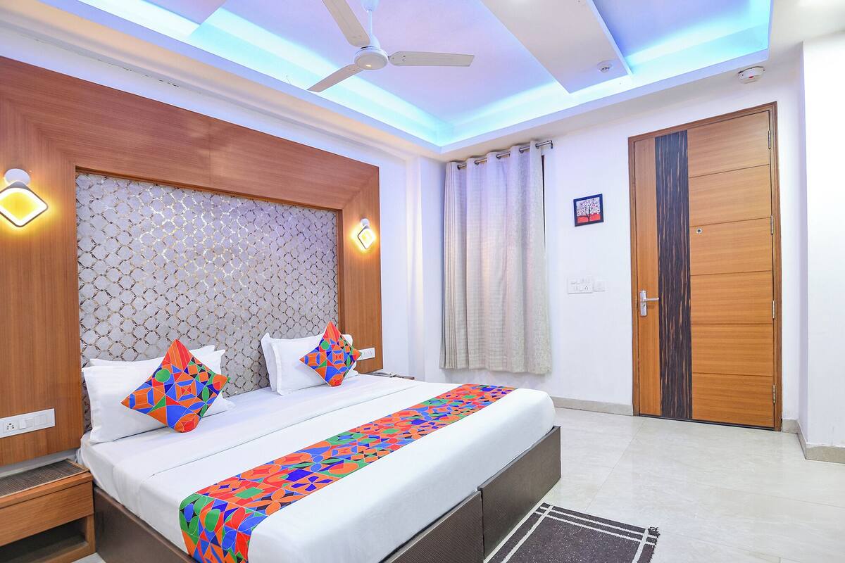A hotel room with a bed, a ceiling fan, a wooden wardrobe, and a bathroom door.