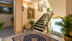 A hotel lobby with a marble staircase, framed artwork, and potted plants. - Fabhotel Prime Familto (Baruipur)